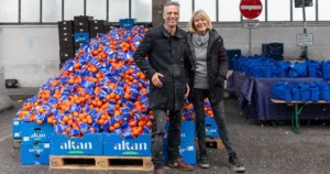 Rocco Bräuniger, Country Manager Amazon Deutschland und Hannelore Kiethe, Vorstandsvorsitzende der Münchner Tafel. Beide stehen vor der Ausgabestelle am Großmarkt, vor vollen Orangenkisten.